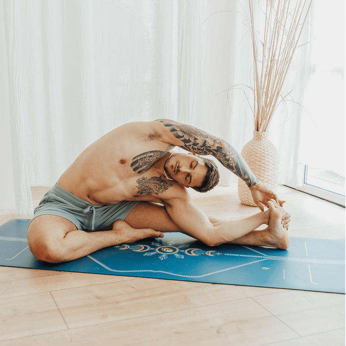 A man performing a yoga stretch on a Liforme Cosmic Moon Blue yoga mat.