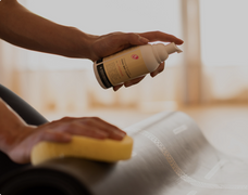 Yogi cleaning their black Liforme Yoga Mat with the Liforme Yoga Mat Cleaner and a soft sponge.