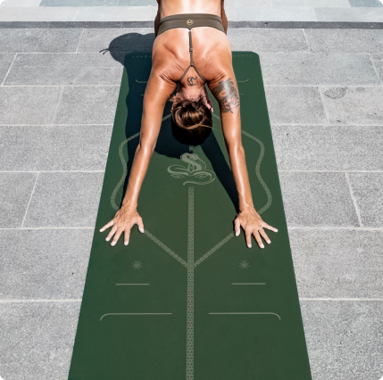 A woman in a Downward-facing dog pose on a Liforme x Jivamukti Yoga Mat Dark Forest Green