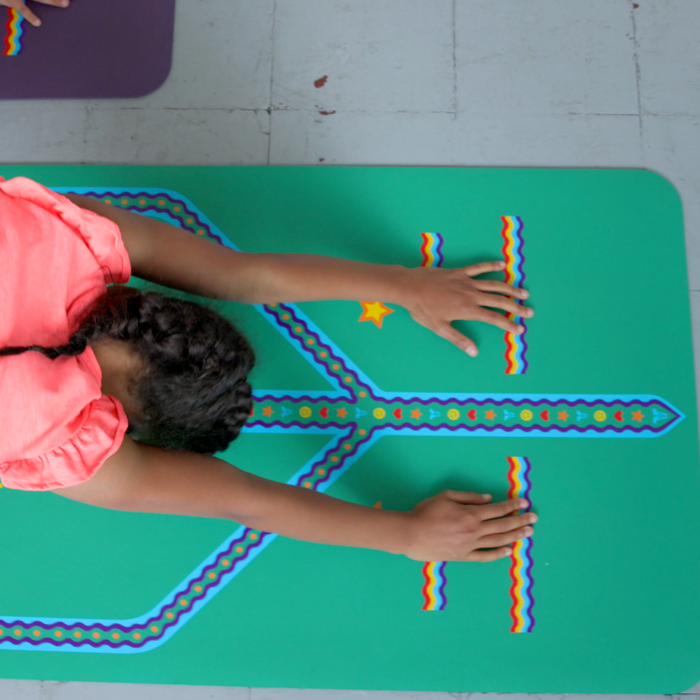 A kid practicing a downward facing dog yoga pose on a Liforme Playful Kids Yoga Mat Green