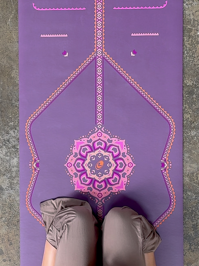 A top-down view of a woman meditating on a Liforme Blossoming Lotus Purple yoga mat.