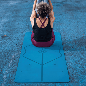 Rear view of a woman in a seated yoga pose with arms raised on a blue Liforme Classic Yoga Mat.
