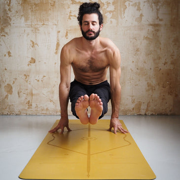 Man performing the Firefly Pose (Tittibhasana) arm balance on a golden sand Liforme Classic Yoga Mat.