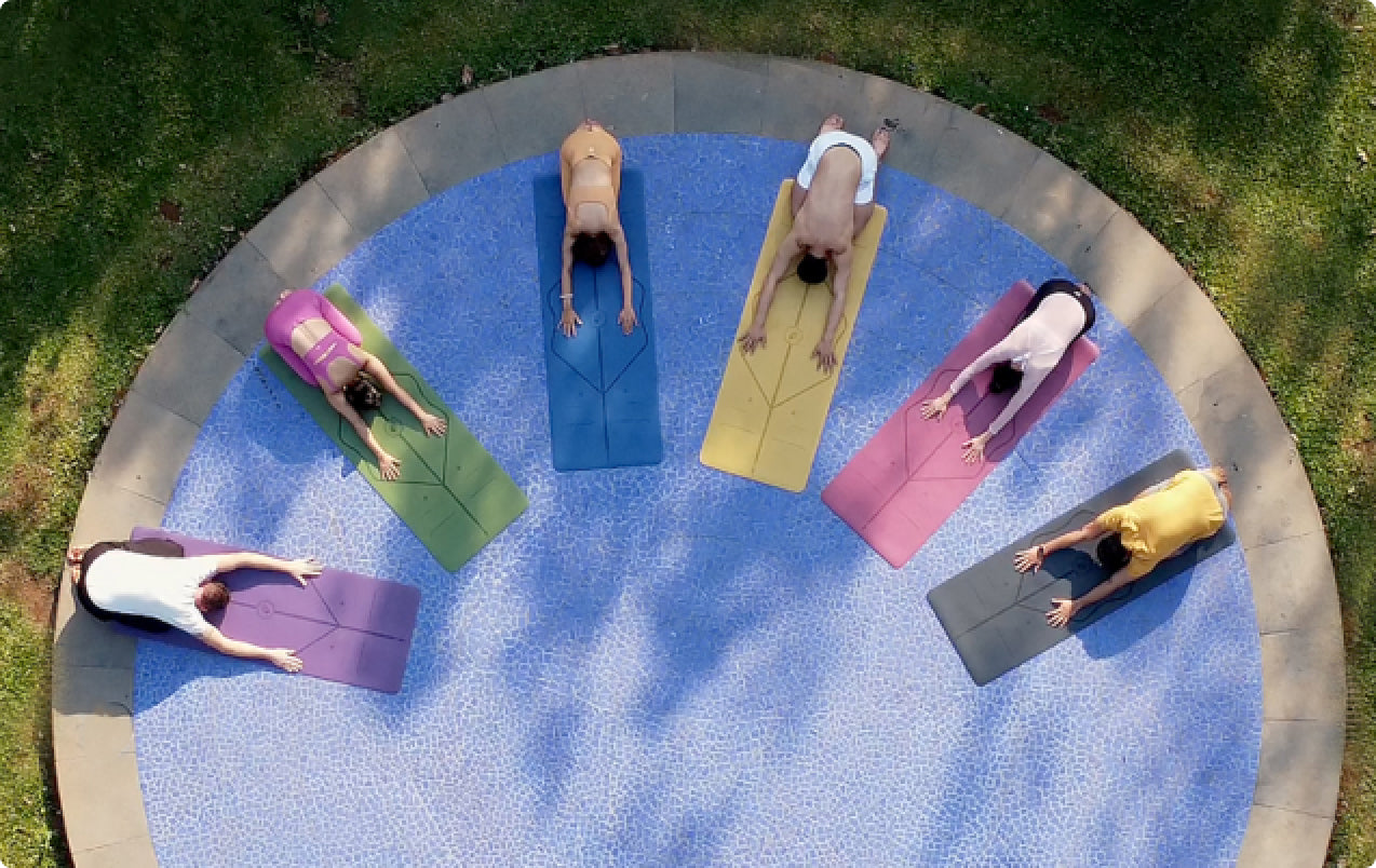 Yogi's practicing Yoga on colourful Liforme Classic Yoga mats in a circular arrangement outdoors.