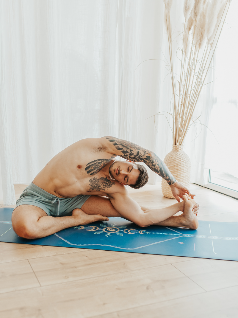 A man performing a yoga stretch on a Liforme Cosmic Moon Blue yoga mat.
