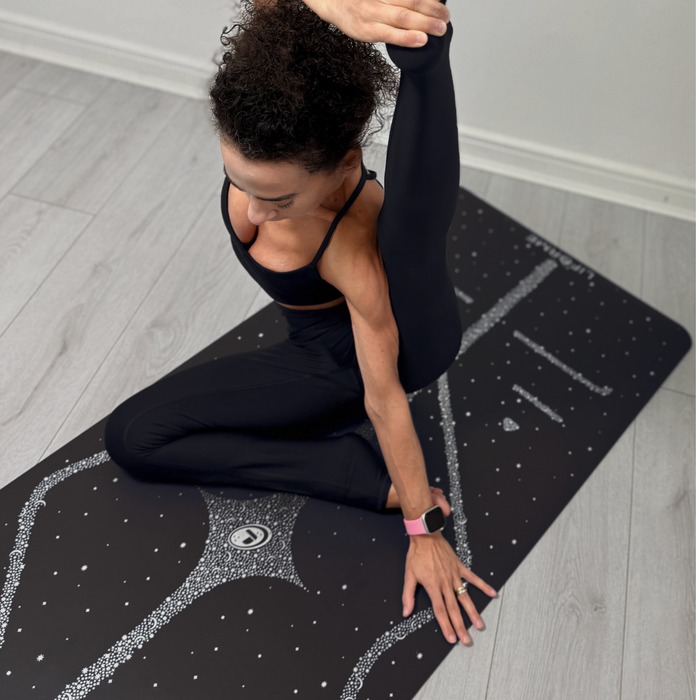 A woman performs a deep yoga pose on a Liforme Magic Galaxy Yoga Mat Silver Black