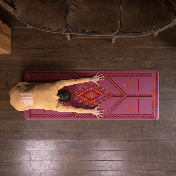 A top-down view of a person performing a child yoga pose on a Liforme Majestic Carpet Maroon