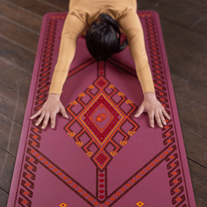  A woman performing a child yoga pose on a Liforme Majestic Carpet Maroon
