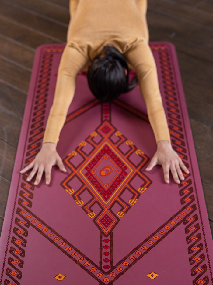  A woman performing a child yoga pose on a Liforme Majestic Carpet Maroon