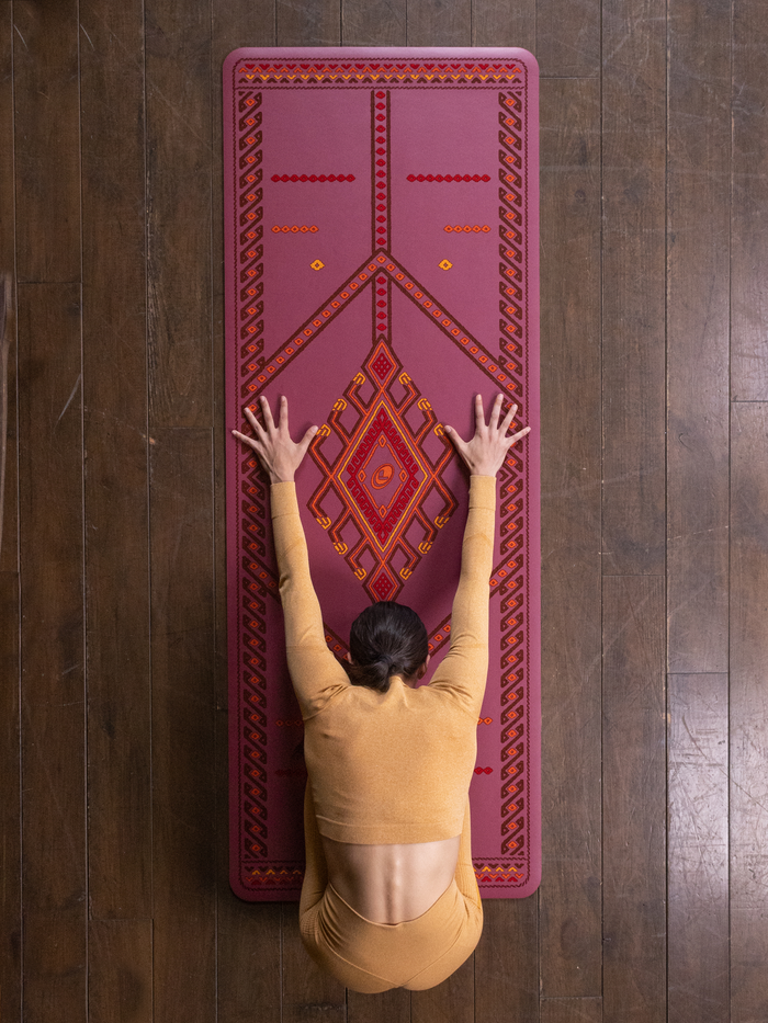 A top-down view of a person performing a child yoga pose on a Liforme Majestic Carpet Maroon
