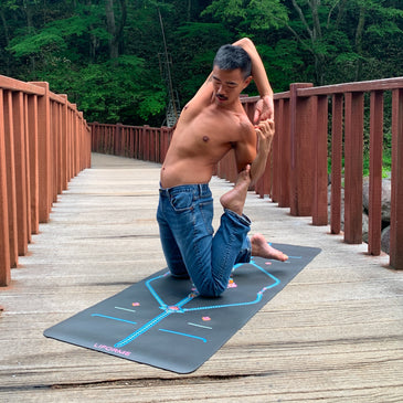 Yoga practitioner in a kneeling stretch on a Liforme Mindful Garden Mat on a forest boardwalk.