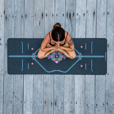 Top-down view of a woman meditating on a grey Liforme Mindful Garden Yoga Mat with colorful alignment guides.