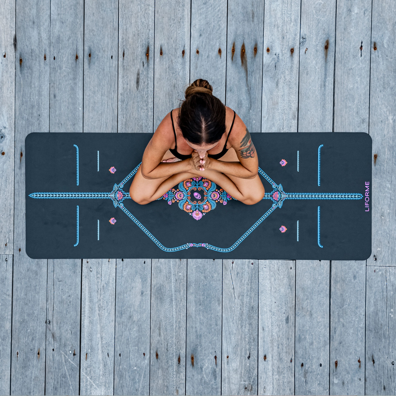 Top-down view of a woman meditating on a grey Liforme Mindful Garden Yoga Mat with colorful alignment guides.