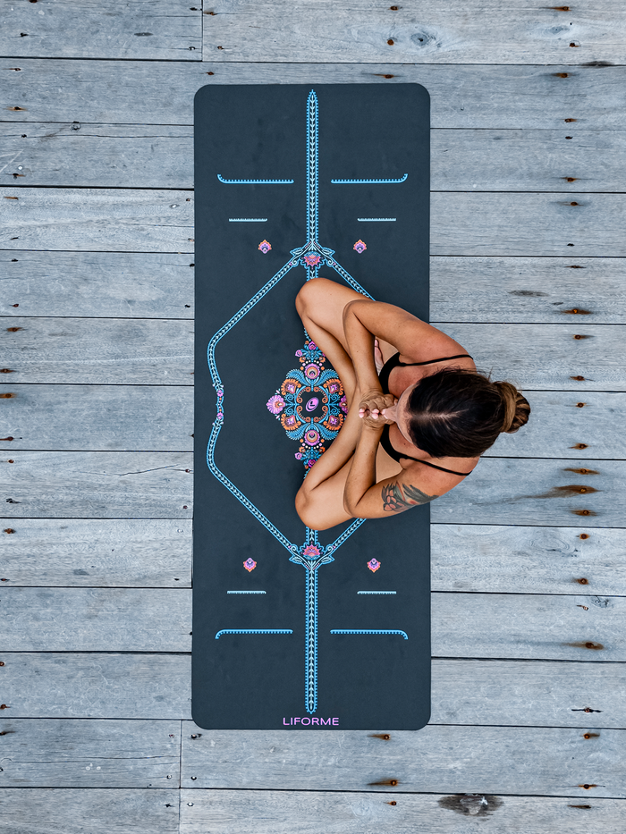Top-down view of a woman meditating on a grey Liforme Mindful Garden Yoga Mat with colorful alignment guides.
