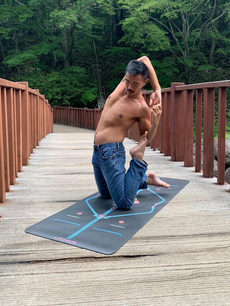 Yoga practitioner in a kneeling stretch on a Liforme Mindful Garden Mat on a forest boardwalk.