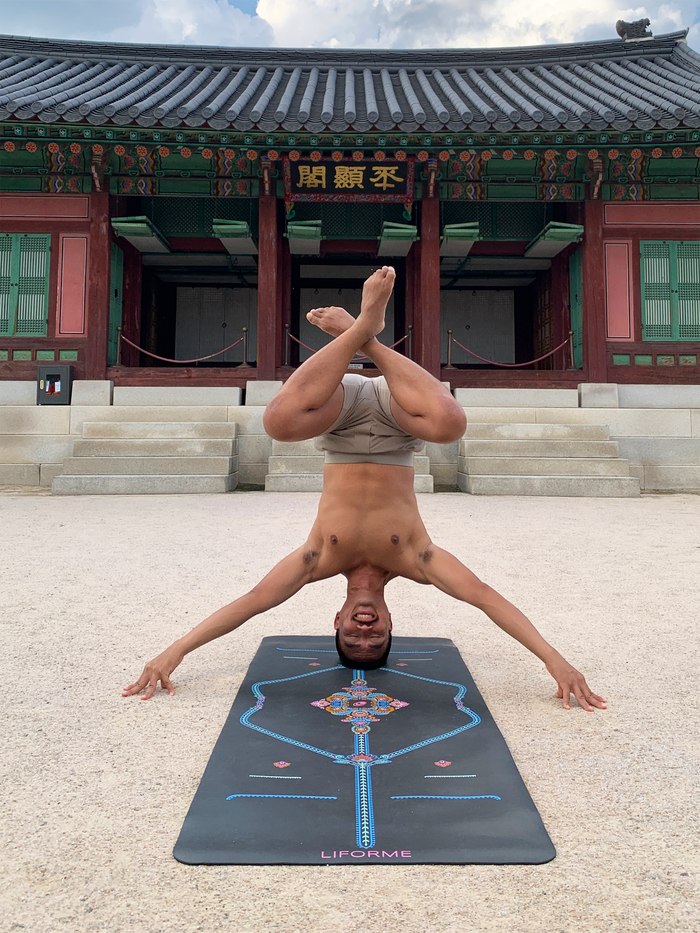Man practicing a lotus headstand on a grey Liforme Mindful Garden Mat at a traditional outdoor temple.