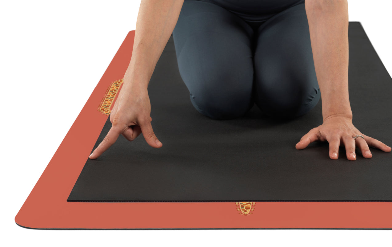 Person in a kneeling position on a black yoga mat with a terracotta liforme mat underneath showing the larger size.