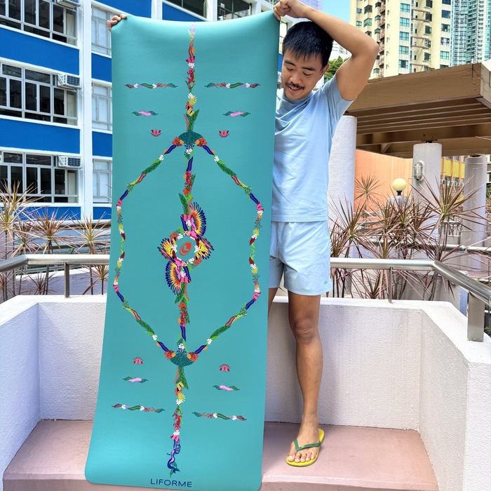 Yogi holding up a Aqua Teal Liforme Tropical Yoga Mat to display the full, colourful tropical alignment design in an outdoor setting.