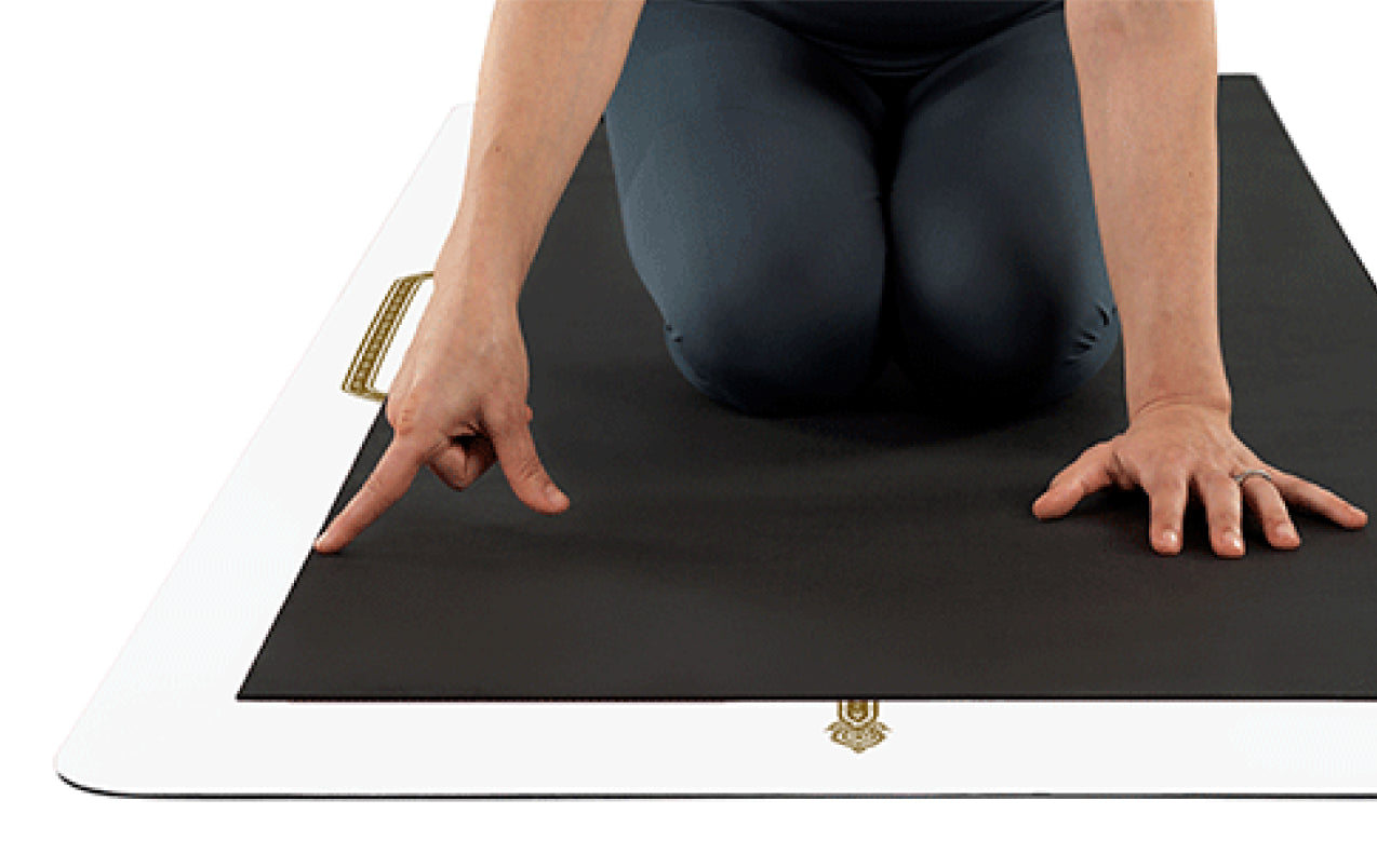 Person in a kneeling position on a black yoga mat with a white liforme mat underneath showing the larger size.