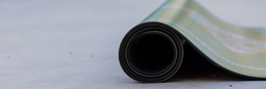 Rolled up Green Lifome Yoga Mat on a grey concrete floor showing the thickness of the mat. 